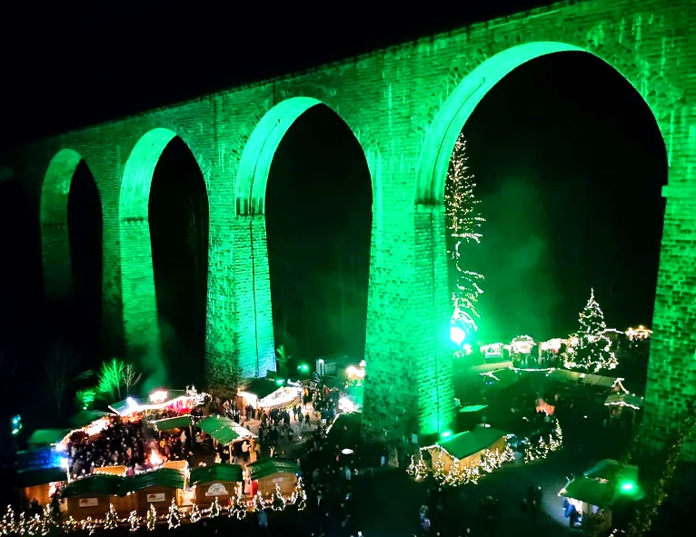 Grün beleuchtete Bögen des Ravenna-Viadukts über dem Weihnachtsmarkt von oben